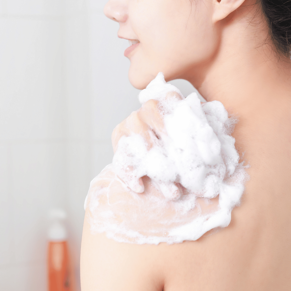 Korean woman lathering soap on her shoulder with a loofah