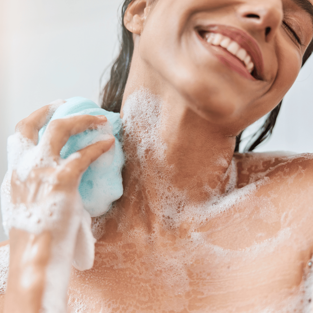 woman lathering soap in shower using a loofah around her neck and shoulders