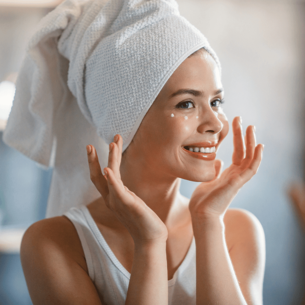 woman in hair towel apllying dots of eye cream around her eyes