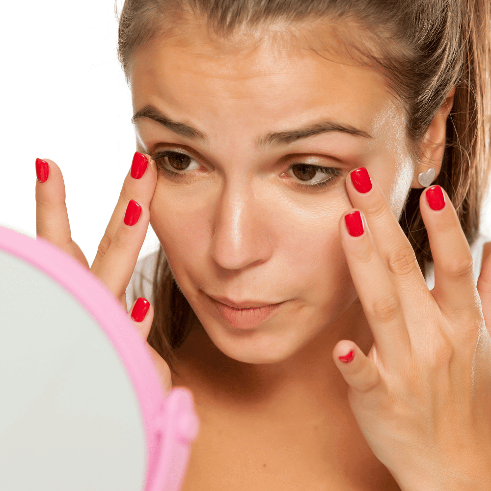 woman carefully and gently putting on eye cream in her mirror
