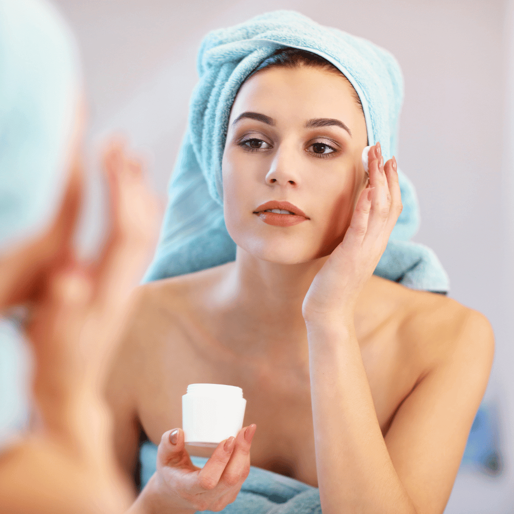 Woman with hair towel on putting on eye cream 